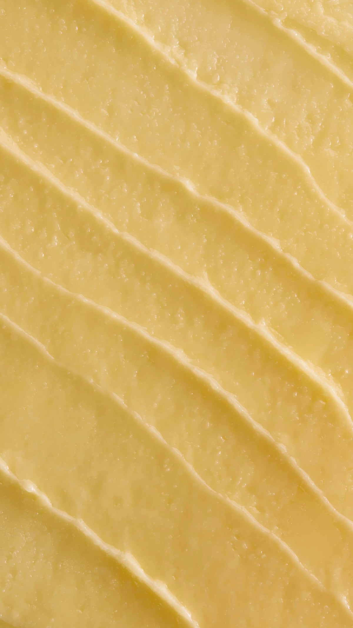 A close-up, aerial shot of thick, pale yellow 'Ultraplant' facial cleanser. The product is spread out in several diagonal, textured ridges, showing its smooth yet slightly granular, buttery consistency.